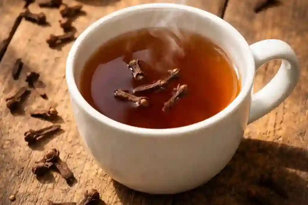 Taza de té de clavo humeante con clavos enteros sobre mesa de madera